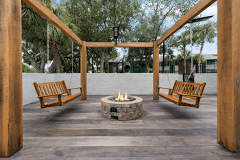 A fire pit is surrounded by two wooden benches and a wooden pergola.
